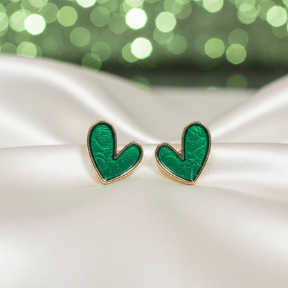Evergreen Heart Earrings on a white satin surface with a blurred green background