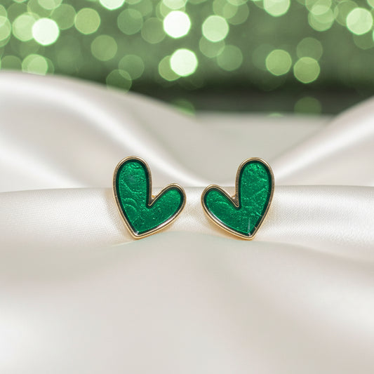 Evergreen Heart Earrings on a white satin surface with a blurred green background