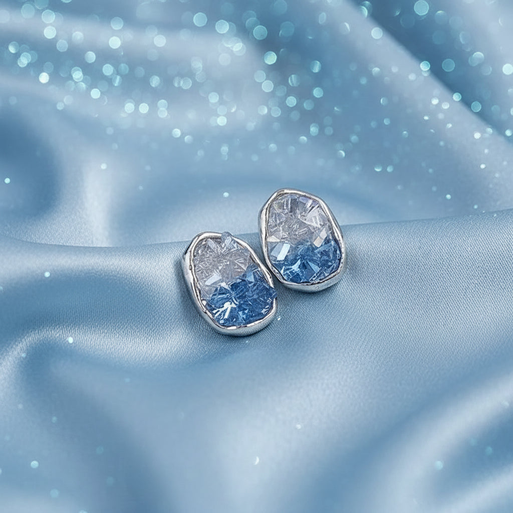 Pair of silver Glacier Blue Crystal Earrings with blue gemstones on a blue satin background