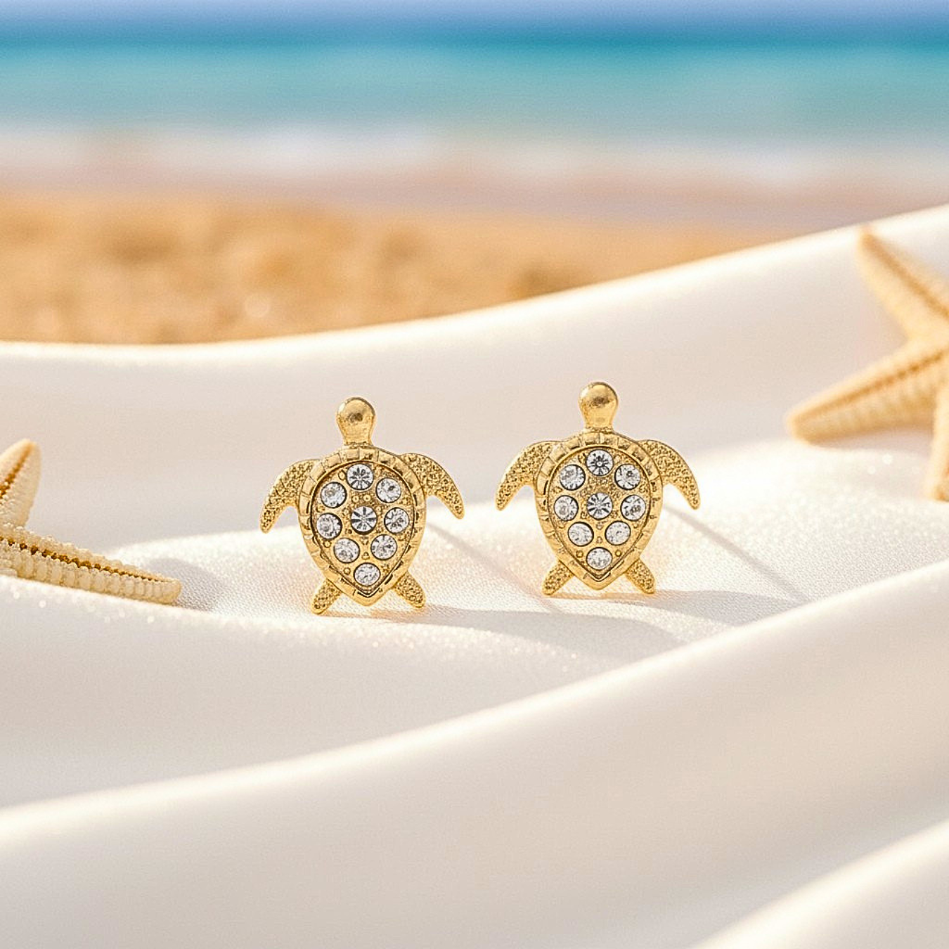 Gold Pavé Sea Turtle Earrings on a sandy surface with starfish.