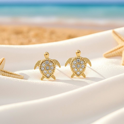 Gold Pavé Sea Turtle Earrings on a sandy surface with starfish.