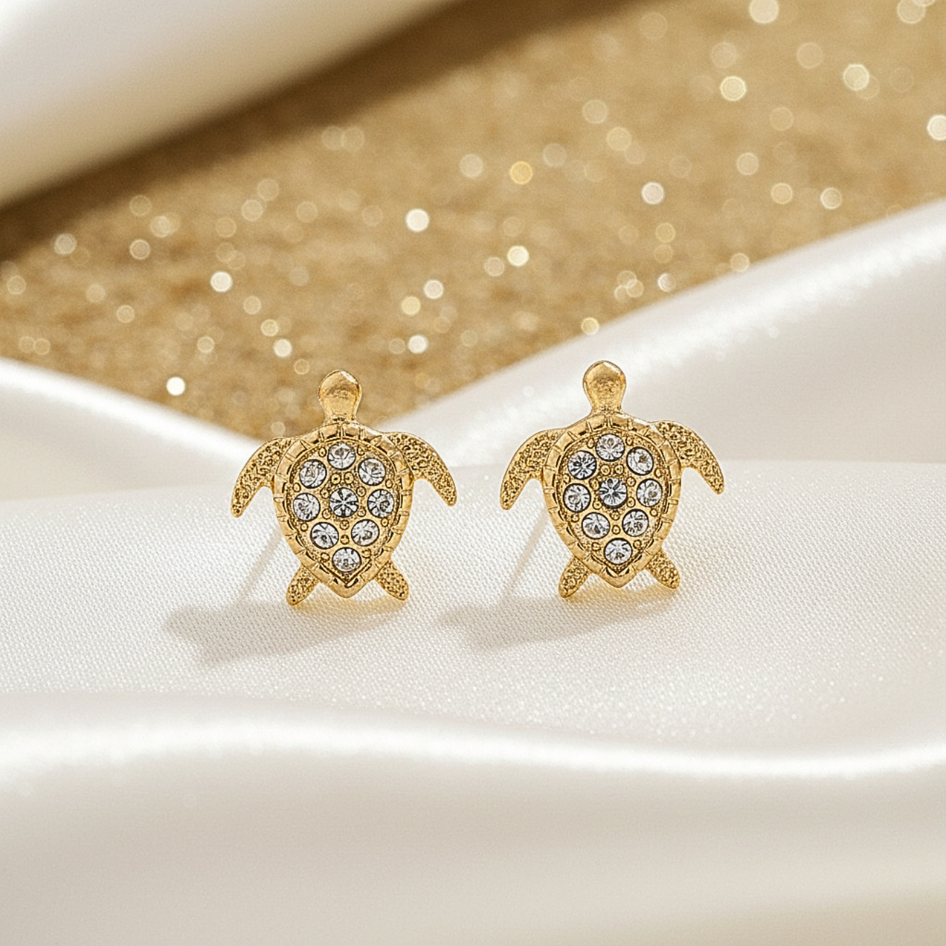 Gold Pavé Sea Turtle Earrings with gemstones on a white and gold glittery background