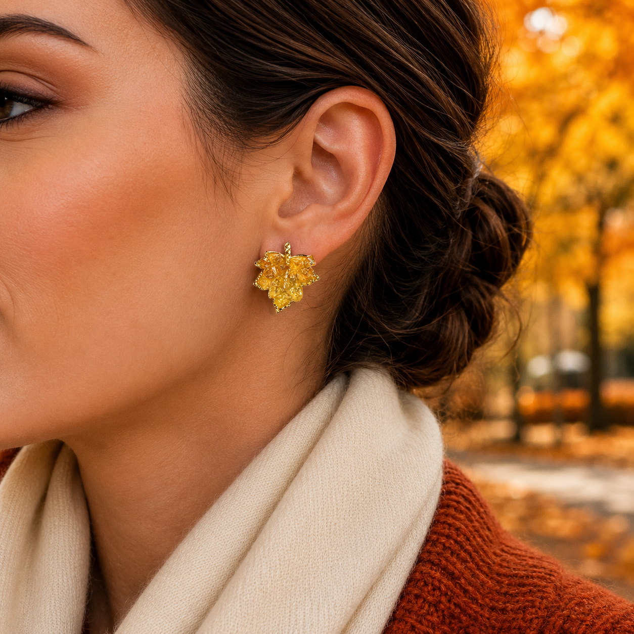 A close-up side profile of a woman wearing a Golden Maple Leaf Earring, set against an autumn park background with golden trees.