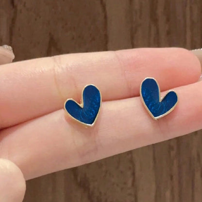 Dark Blue Heart Earrings held between two fingers against a wooden background