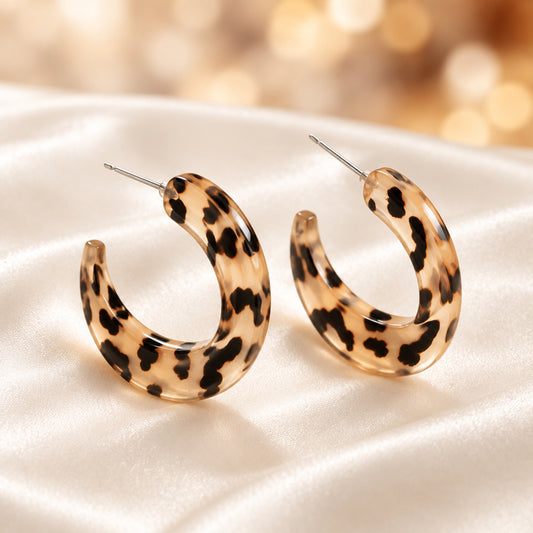 Leopard print hoop earrings on a stone surface with pebbles in the background
