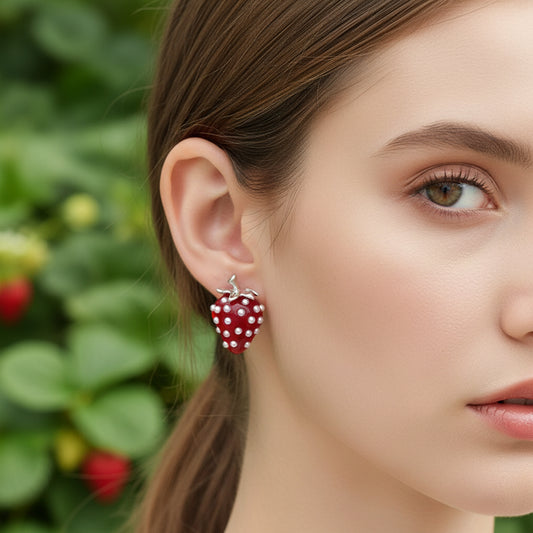 Red strawberry-shaped earrings with pearl-like embellishments on a beige fabric background