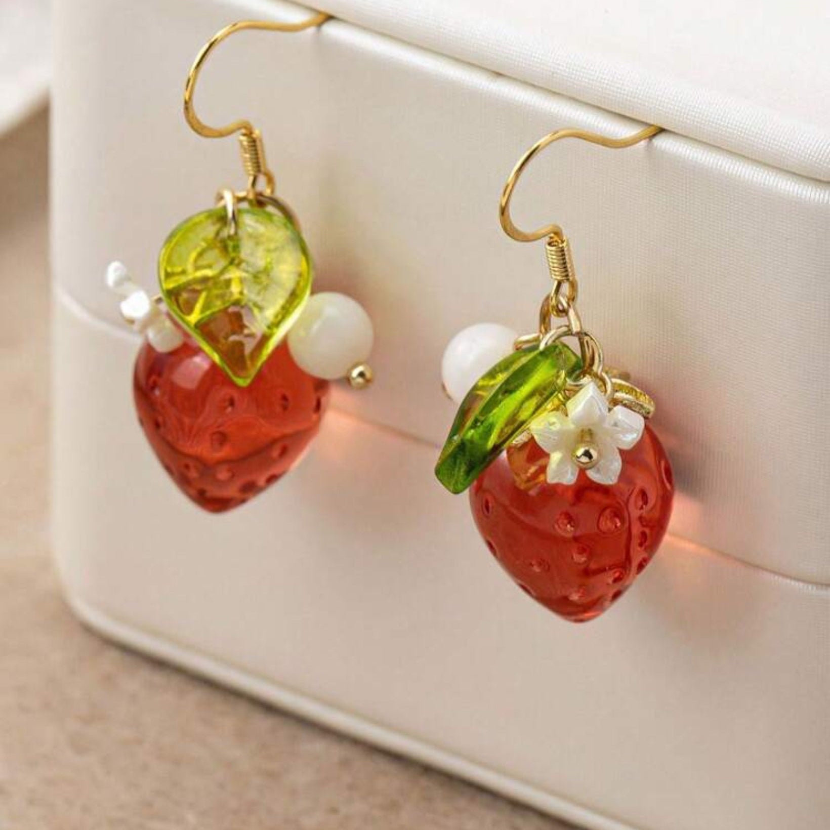 Strawberry Flower Earrings with green leaves and white flowers on a beige surface