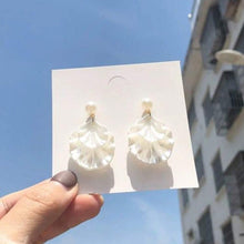 Load image into Gallery viewer, Pearl-like earrings on a card held against a blue sky with buildings in the background
