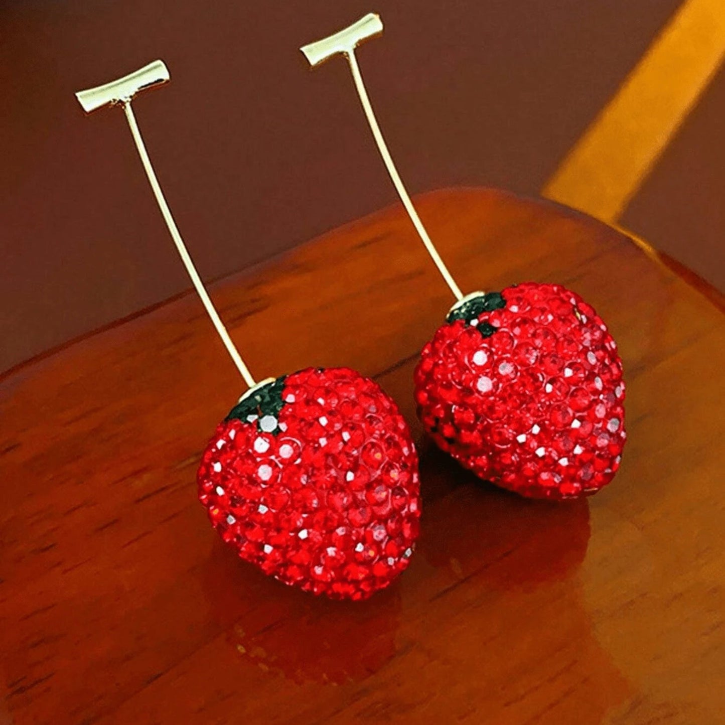 Two red strawberry-shaped objects with rhinestone embellishments on a wooden surface.