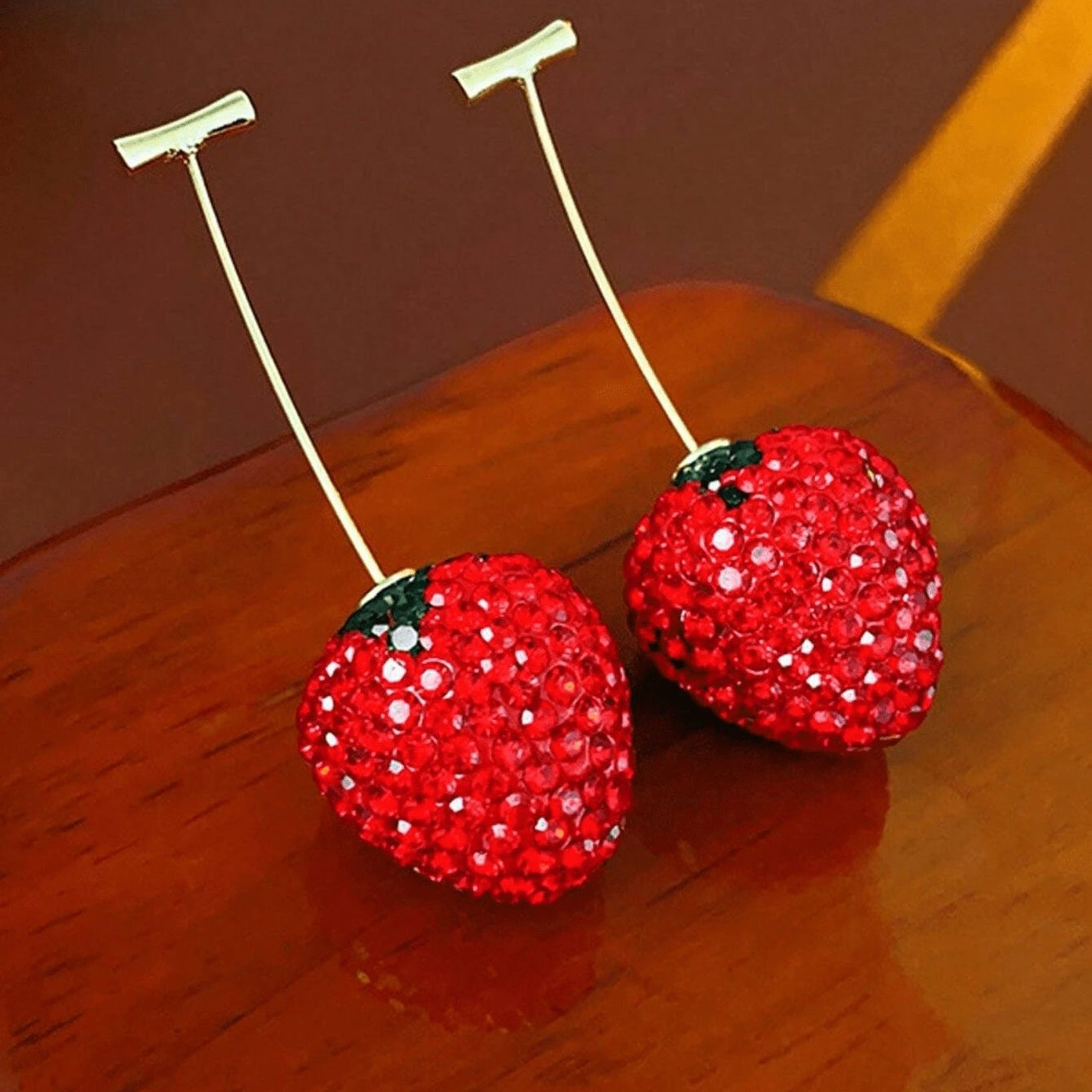 Two red strawberry-shaped objects with rhinestone embellishments on a wooden surface.