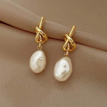 Load image into Gallery viewer, Gold earrings with pearl drops on a beige surface
