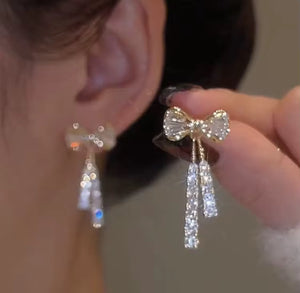 Close-up of a person wearing bow-shaped earrings with dangling crystals.