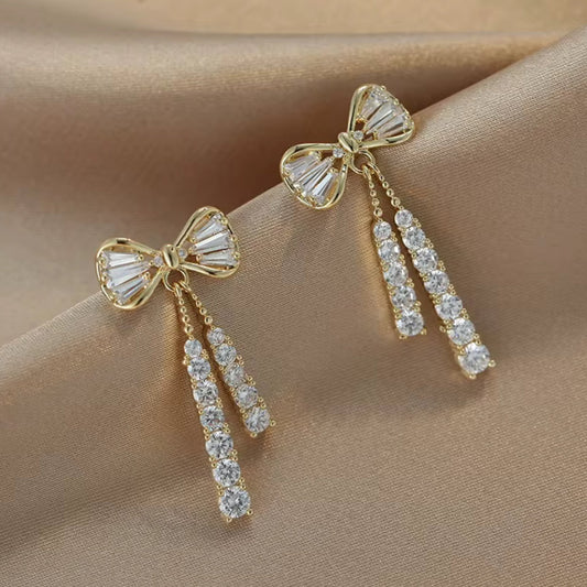 Gold bow-shaped earrings with diamond accents on a beige fabric background