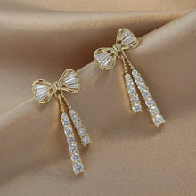 Load image into Gallery viewer, Gold bow-shaped earrings with diamond accents on a beige fabric background
