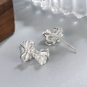 Silver bow-shaped earrings on a light gray surface