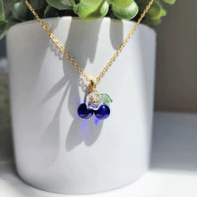 Load image into Gallery viewer, Necklace with blue beads and a leaf charm on a white surface with a plant in the background