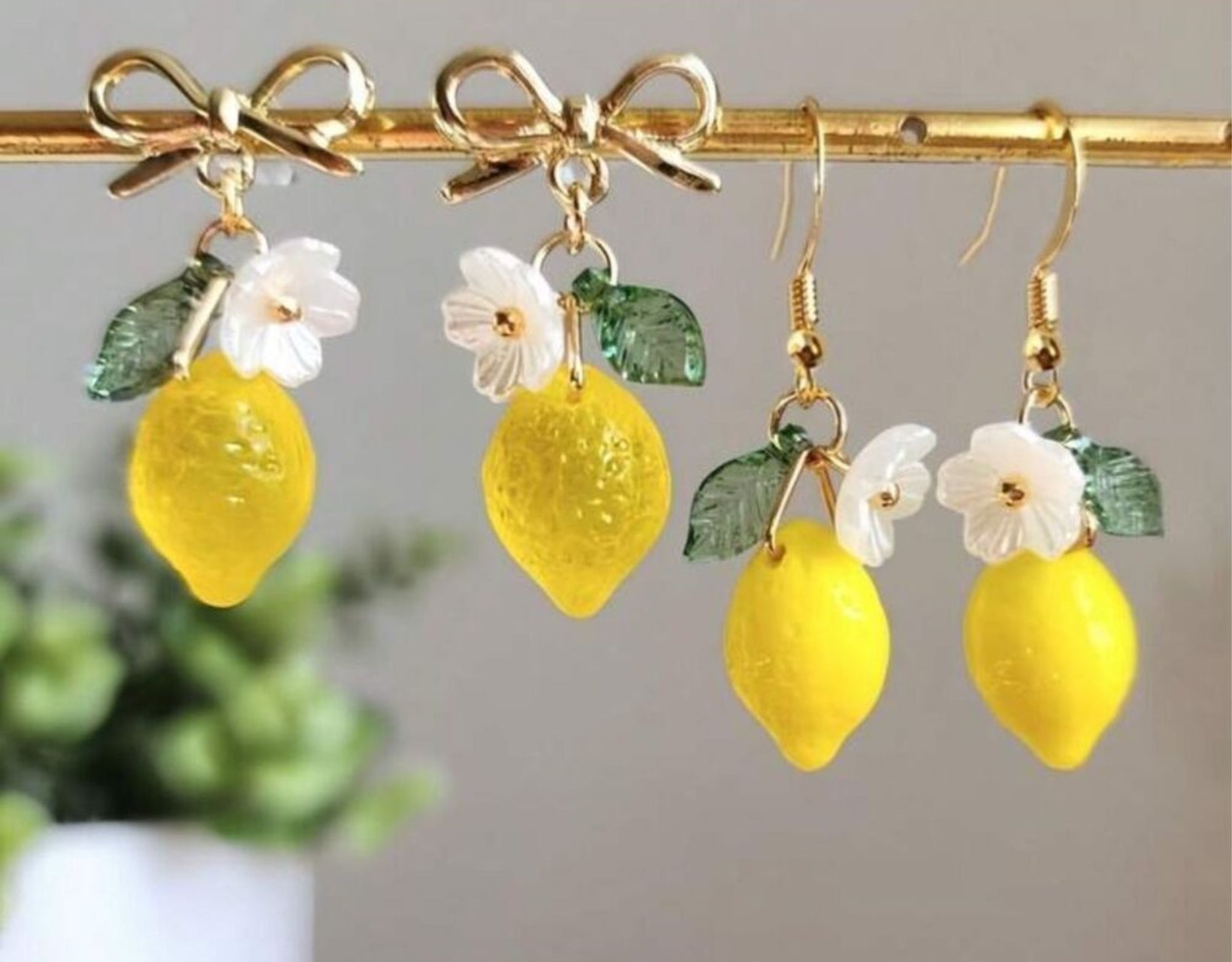 Lemon-shaped earrings with gold hooks, green leaves, and white flowers on a gray background.