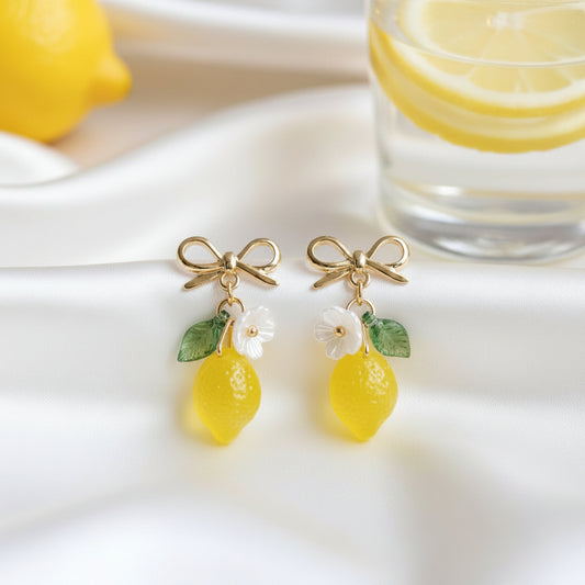 Lemon-shaped earrings with gold hooks, green leaves, and white flowers on a gray background.