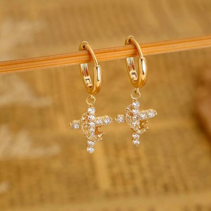 Gold Cross Crown earrings with cubic zirconia stones on a wooden stick against a blurred background