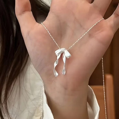 Silver Ribbon Bow Necklace with a bow pendant held by a person