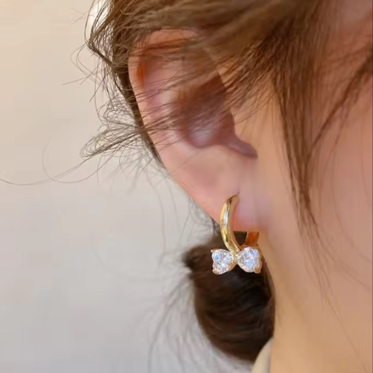Gold Zircon Bow Hoop Earrings with a clear gemstone worn by a person.