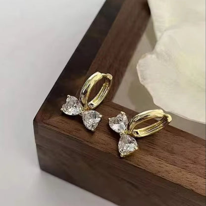 Gold Zircon Bow Hoop Earrings with clear gemstones on a wooden surface