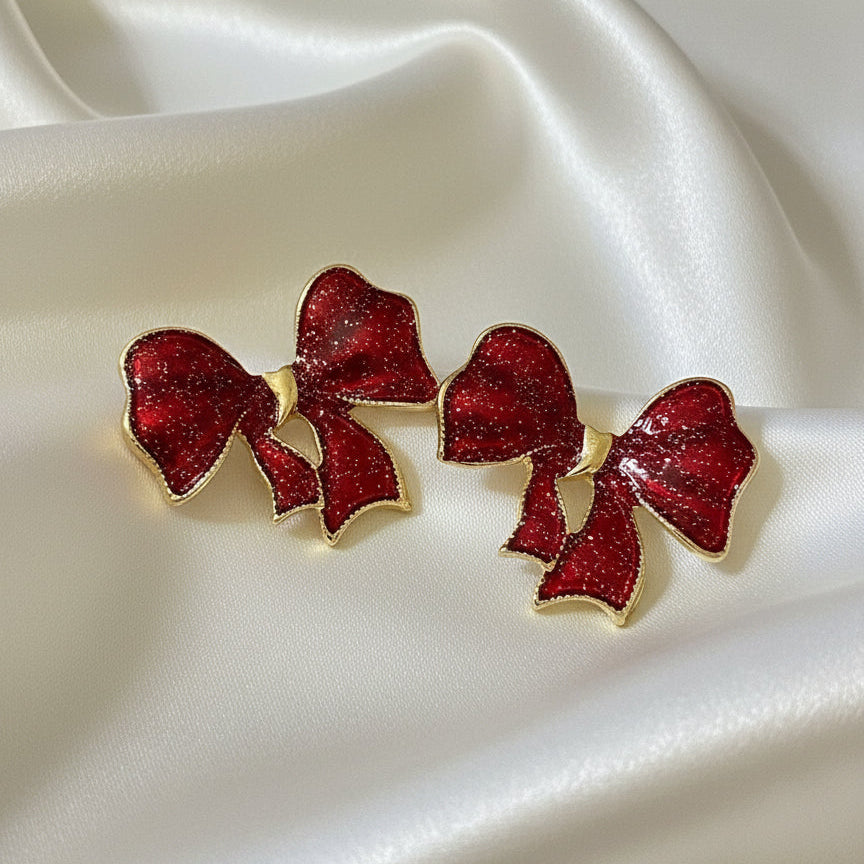 Crimson Glitter Bow Earrings on a white satin background