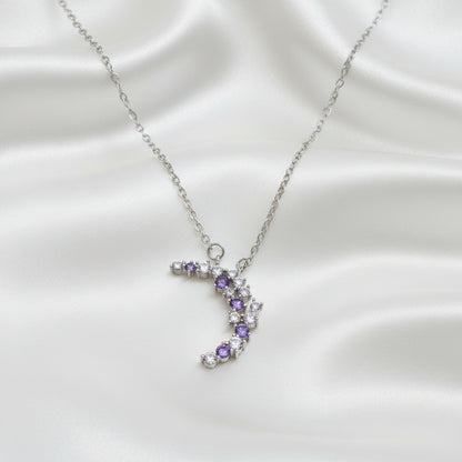 Purple & Silver Crescent Moon Necklace with purple and clear gemstones on a light blue background