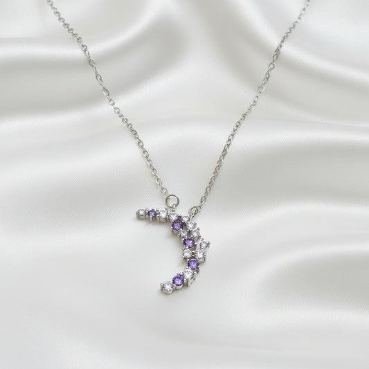 Purple & Silver Crescent Moon Necklace with purple and clear gemstones on a light blue background