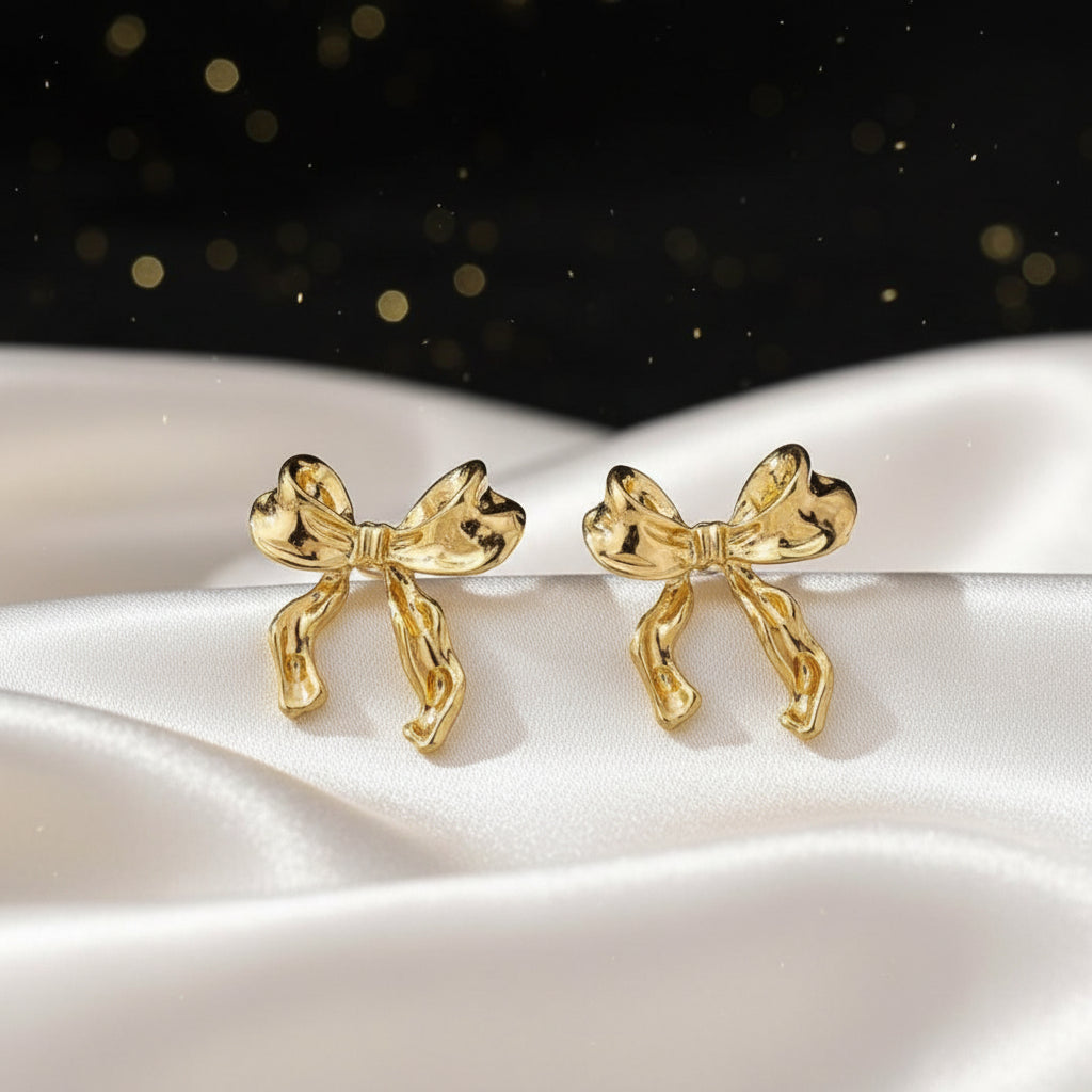 Gold Bow Ribbon Earrings on a white surface with a dark, sparkling background