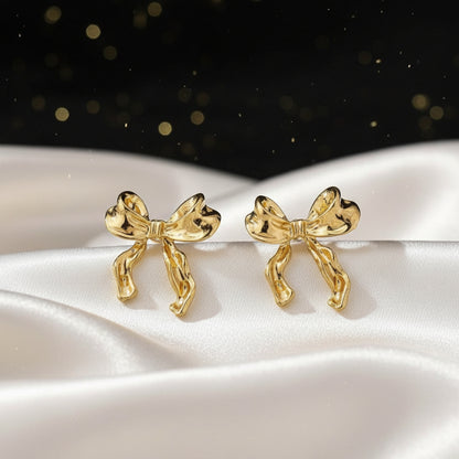 Gold Bow Ribbon Earrings on a white surface with a dark, sparkling background