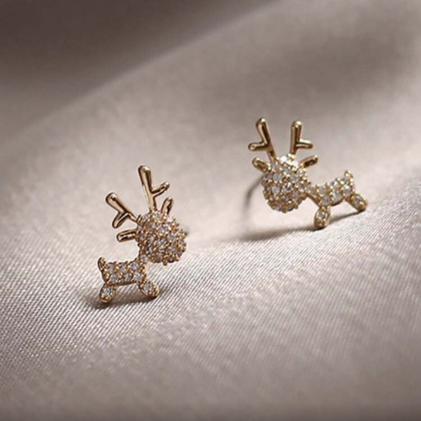 Zircon Deer Earrings with diamond-like stones on a light fabric background