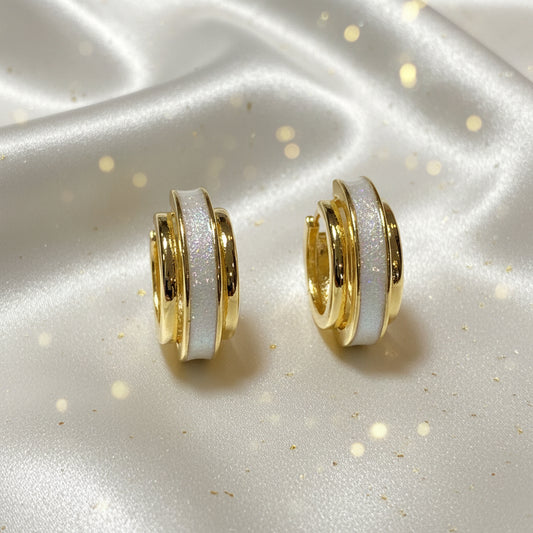 Gold Dust White & Gold Huggie Earrings with white glittery centers on a satin surface