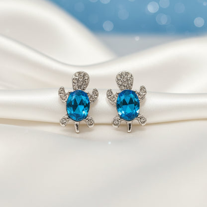Ocean Blue Crystal Turtle Earrings with blue gemstones on a white surface with a blue background