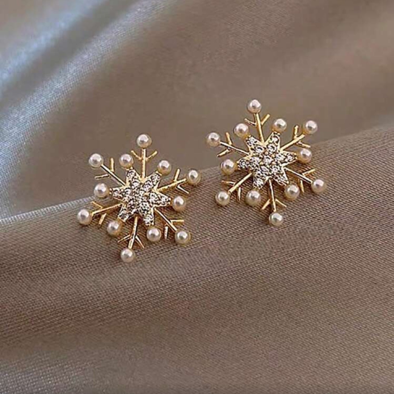Snowflake Pearl Earrings with pearl accents on a beige fabric background