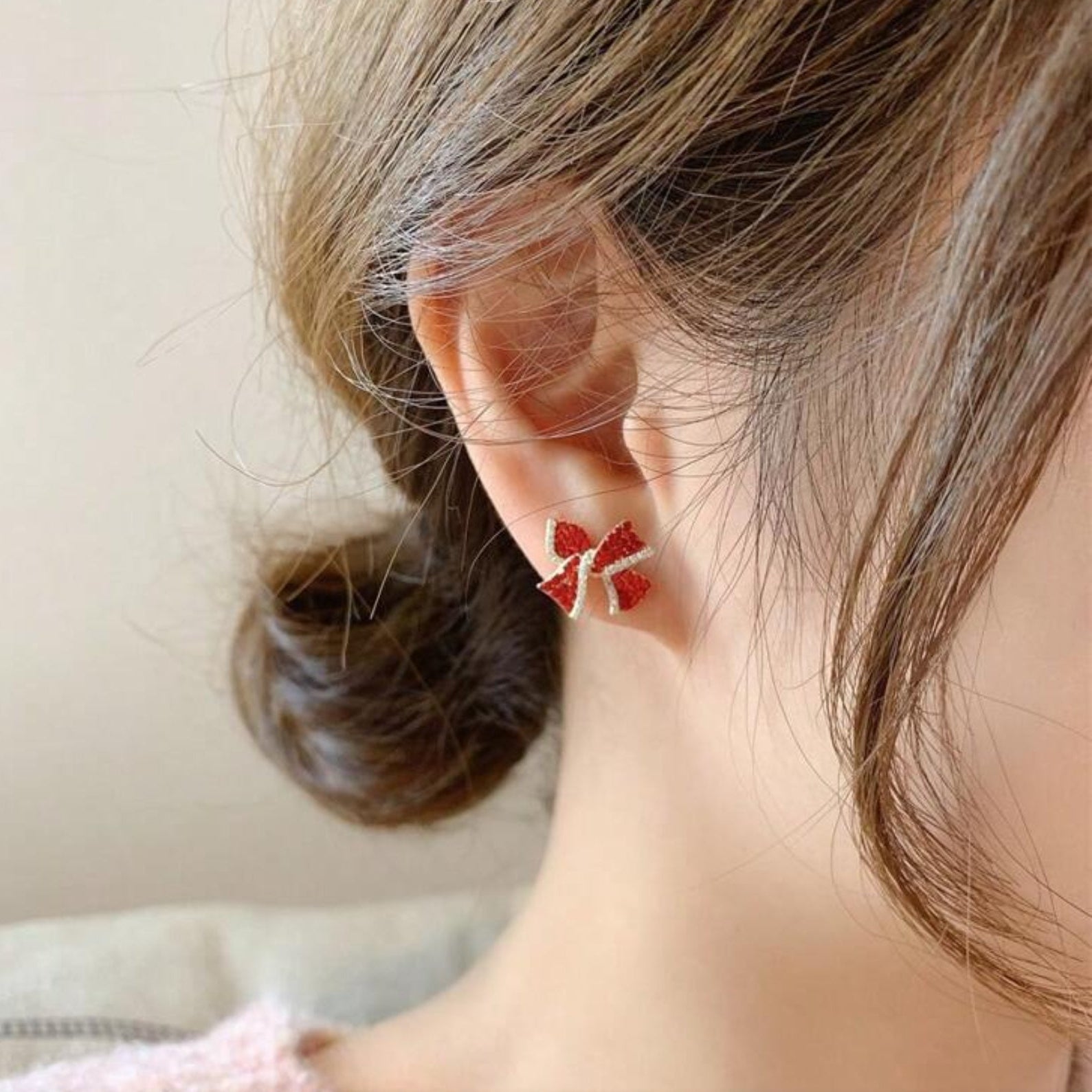 Close-up of an ear wearing Red Bow Earrings with a neutral background