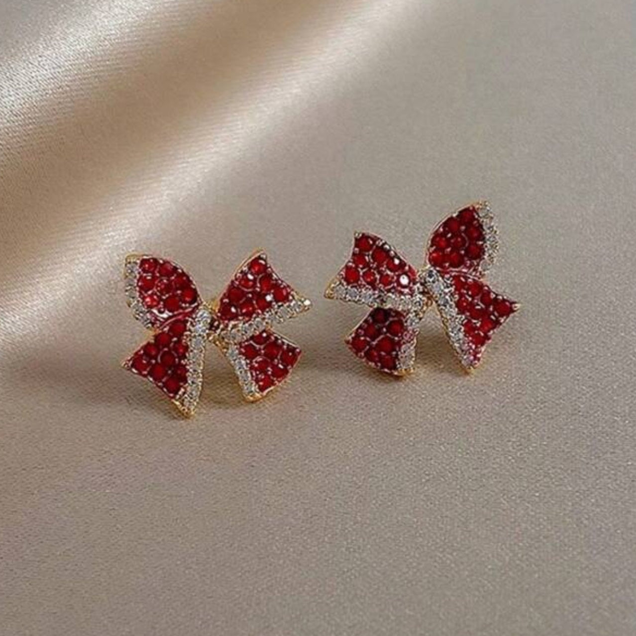 Red Bow Earrings with red gemstones on a beige fabric background