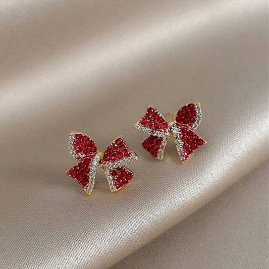 Red Bow Earrings with red gemstones on a beige fabric background