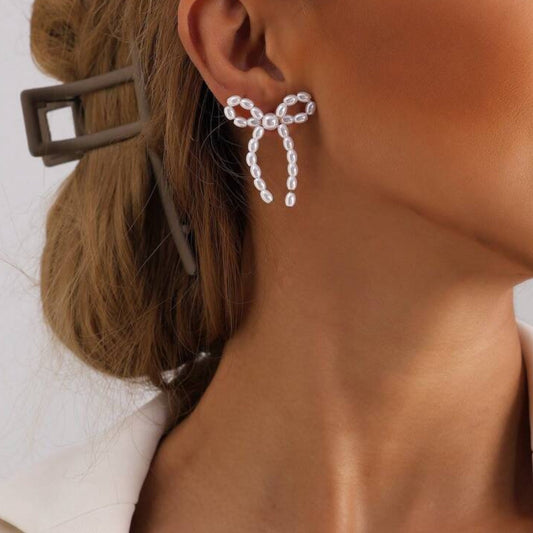 Close-up of a person wearing Pearl Bow Earrings with a neutral background