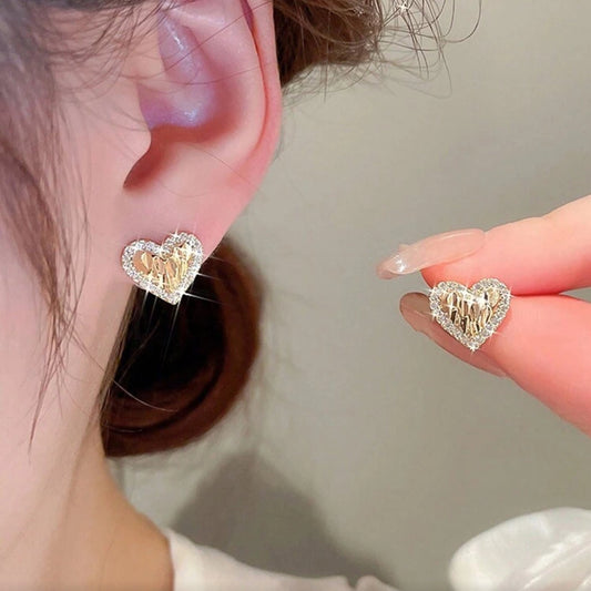 Gold Shimmer Heart Earrings being worn and held up to the ear.