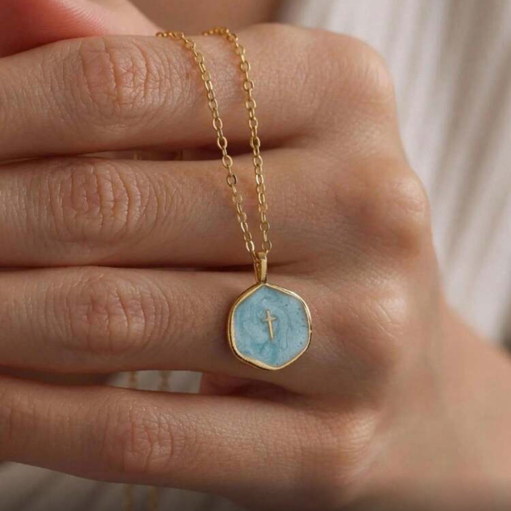 Walk in Faith Enamel Cross Necklace with a blue pendant held by a hand