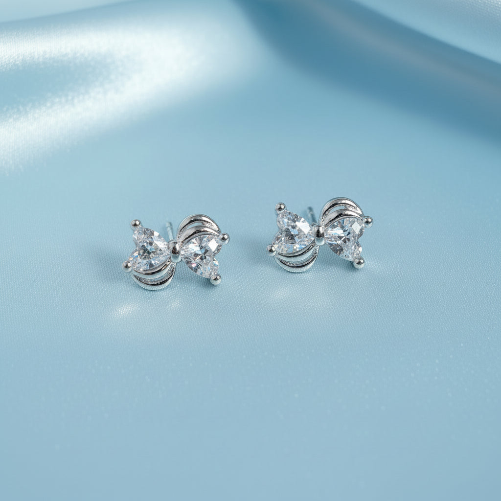 Mini Silver Heart Crystal Bow Earrings with heart-shaped gemstones on a light blue background
