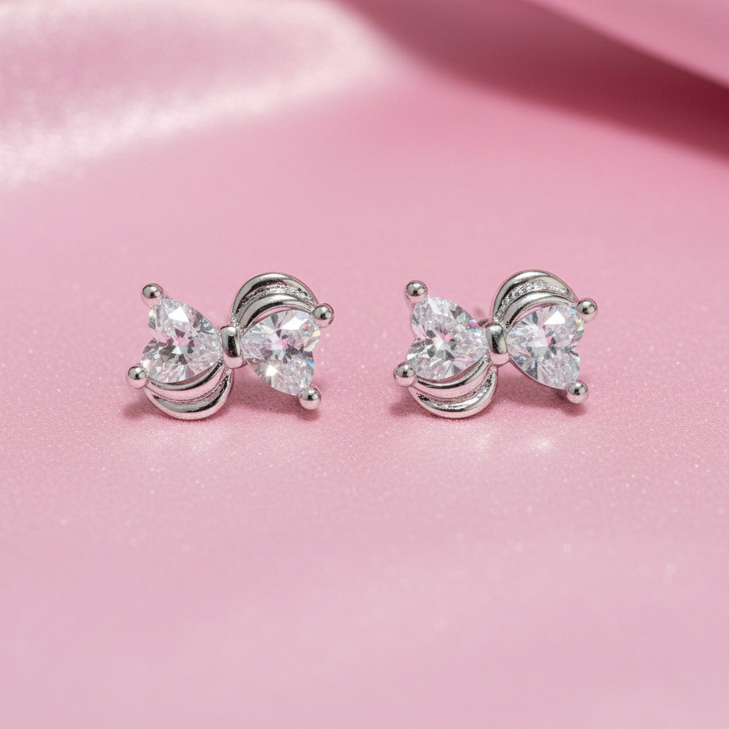 Mini Silver Heart Crystal Bow Earrings with clear gemstones on a pink background