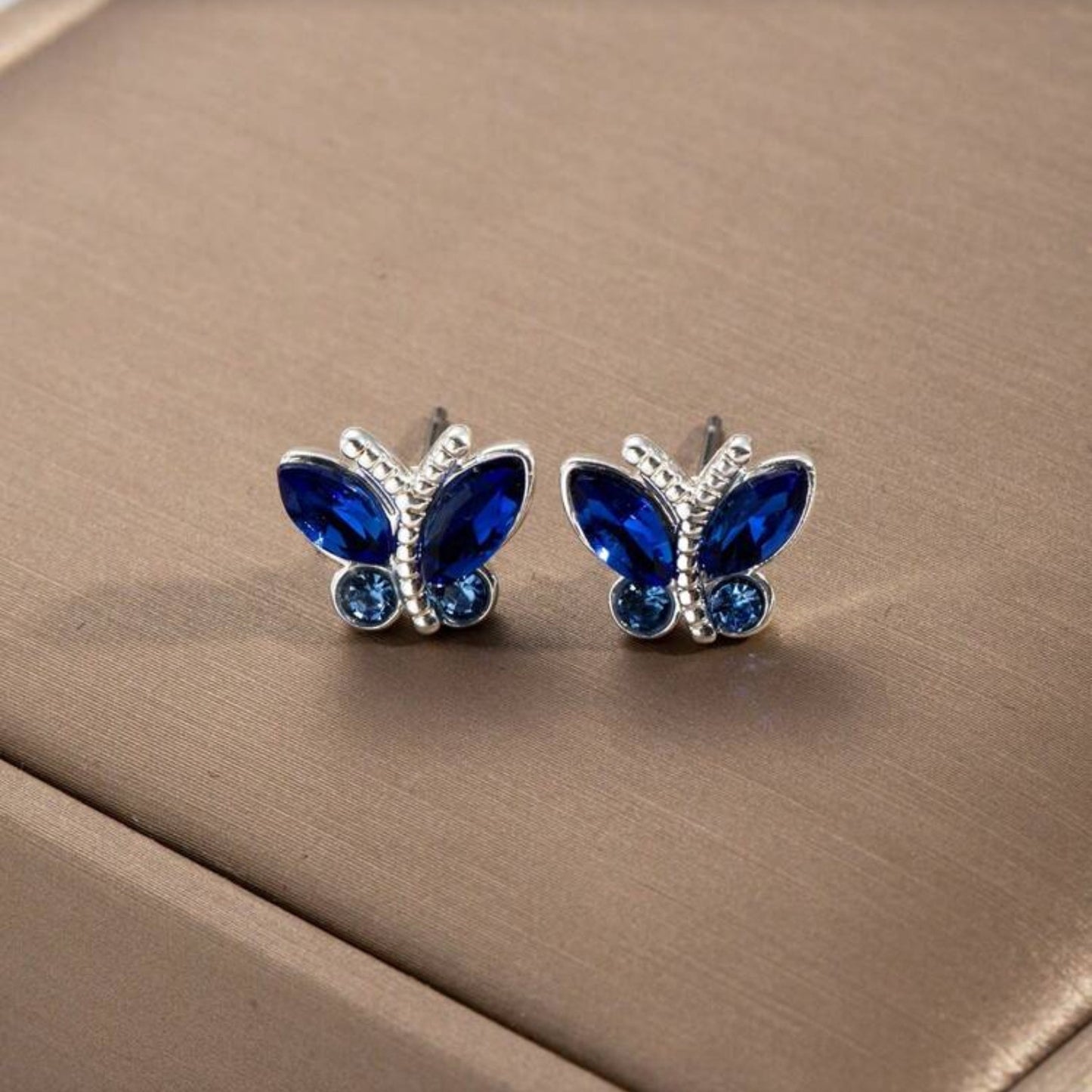 Midnight Blue Butterfly Stud Earrings on a beige surface