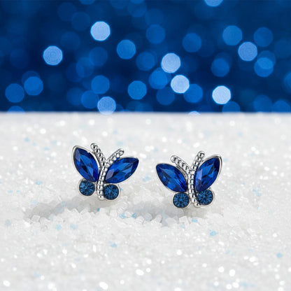 Midnight Blue Butterfly Stud Earrings with blue gemstones on a white surface with a blue bokeh background