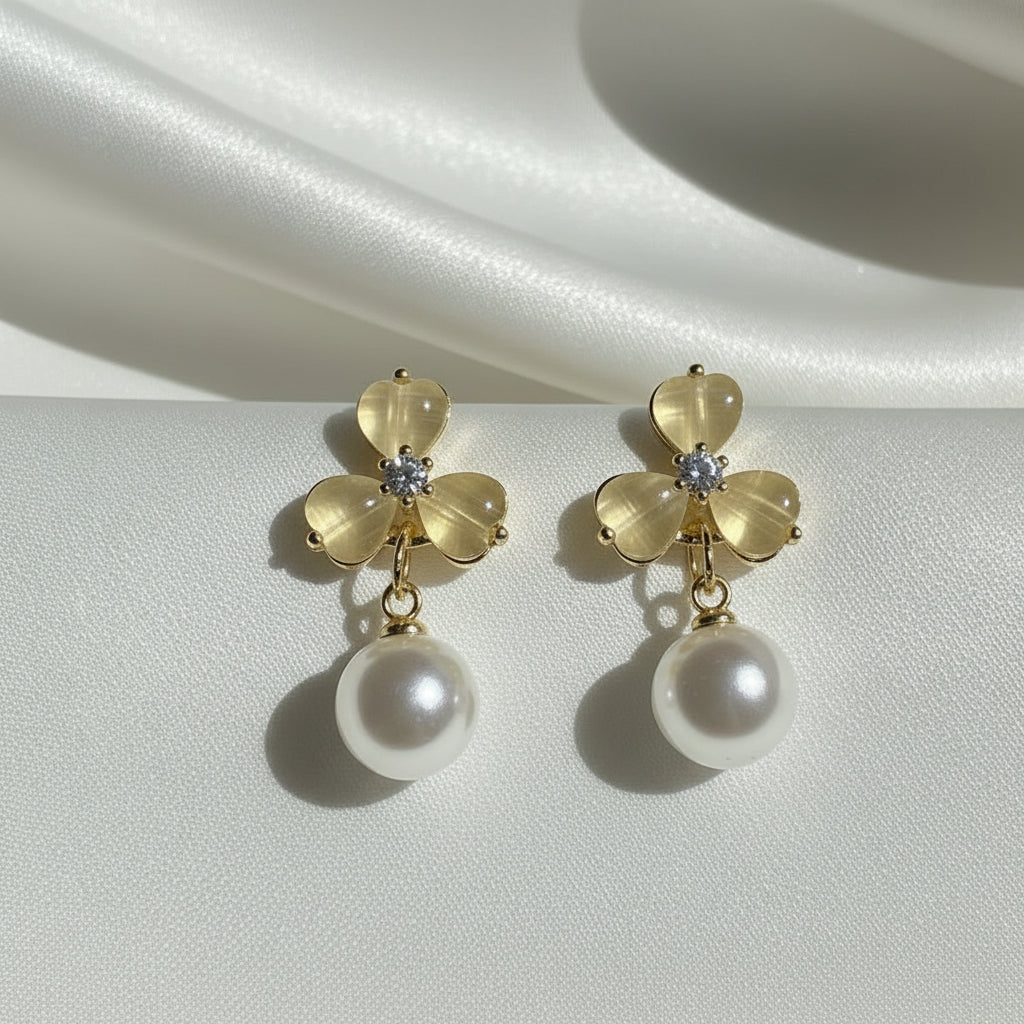Luminous Gold Clover Pearl Drop Earrings on a satin surface