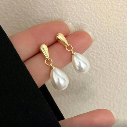 Gold Pearl Teardrop Earrings held between fingers against a neutral background