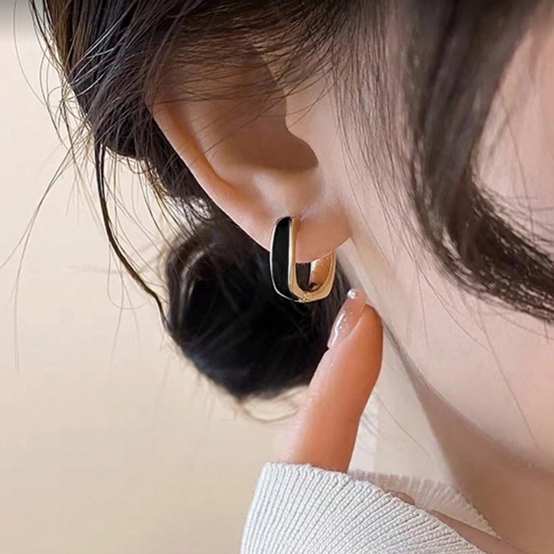 Close-up of a woman wearing a Black Enamel Hoop Earrings with a neutral background