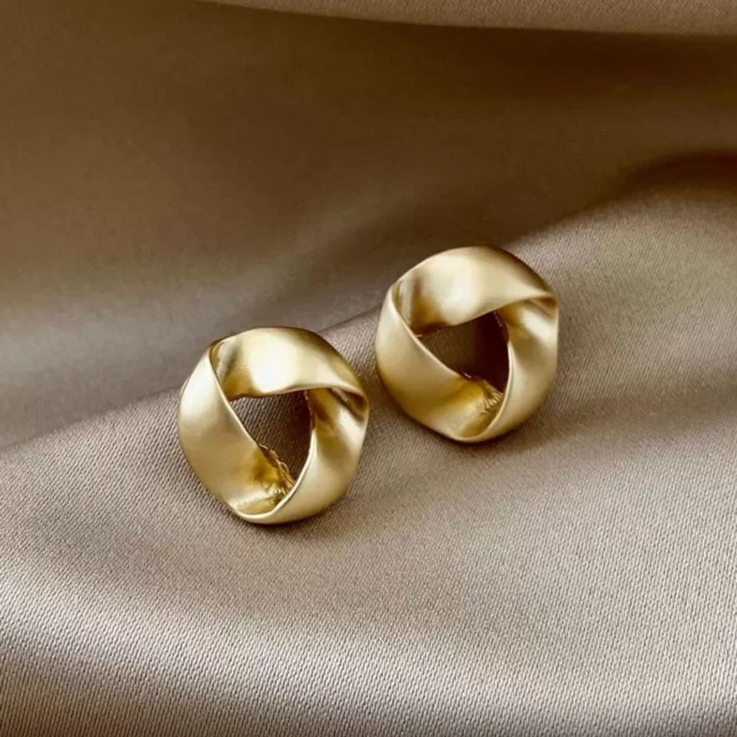 Pair of satin gold knot earrings on a beige fabric background
