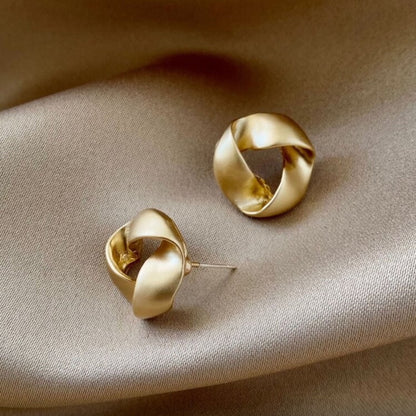 Pair of satin gold knot earrings on a beige fabric background